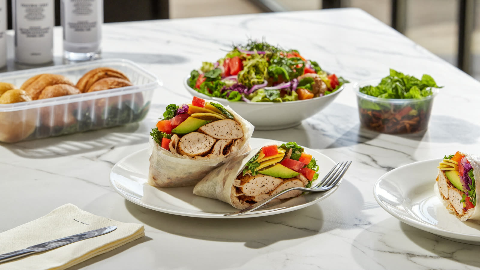 Fresh gourmet wraps cut open beside a vibrant rainbow garden salad on a clean marble bench